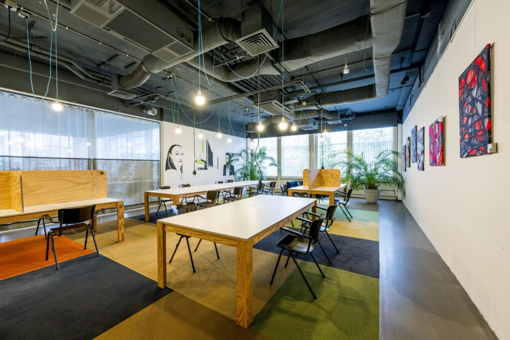 Modern co-working space on Laan van Kronenburg with wooden desks, colorful wall art, and large windows offering natural light.
